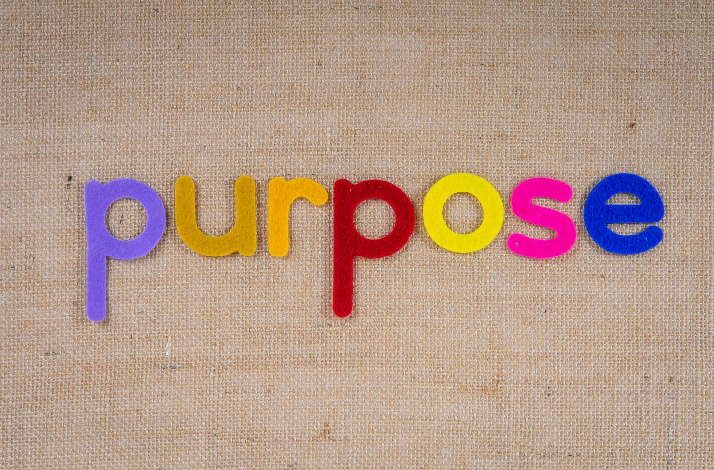 The word purpose spelled out in multi-coloured felt letters on a brown cloth background